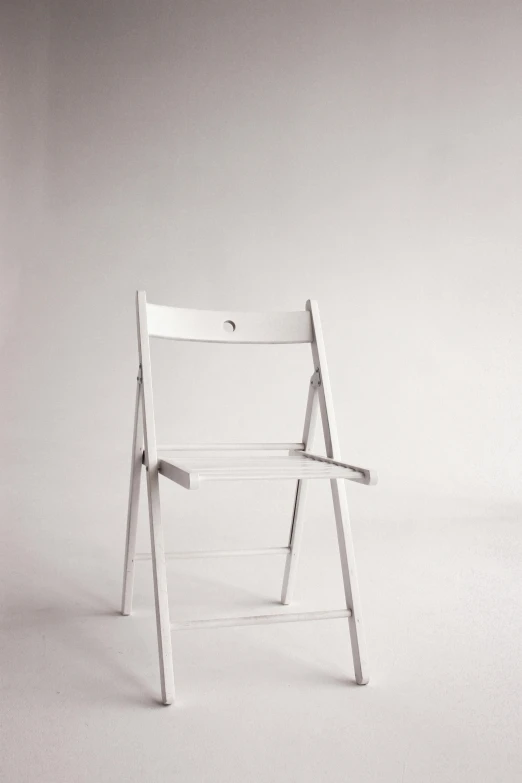 a white chair sits alone in a minimal, empty studio environment