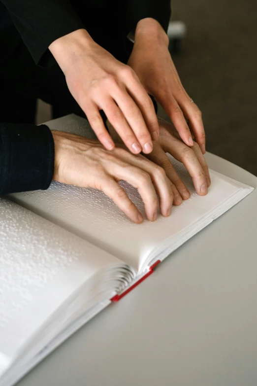 two hands on top of a book with one hand reaching for the book