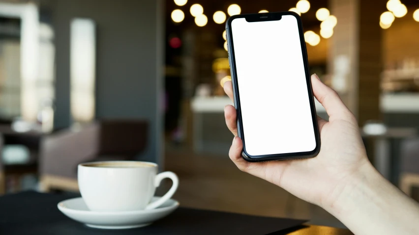 person holding cell phone in front of empty plate and cup on table