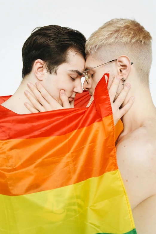 two guys hugging each other behind a rainbow colored flag