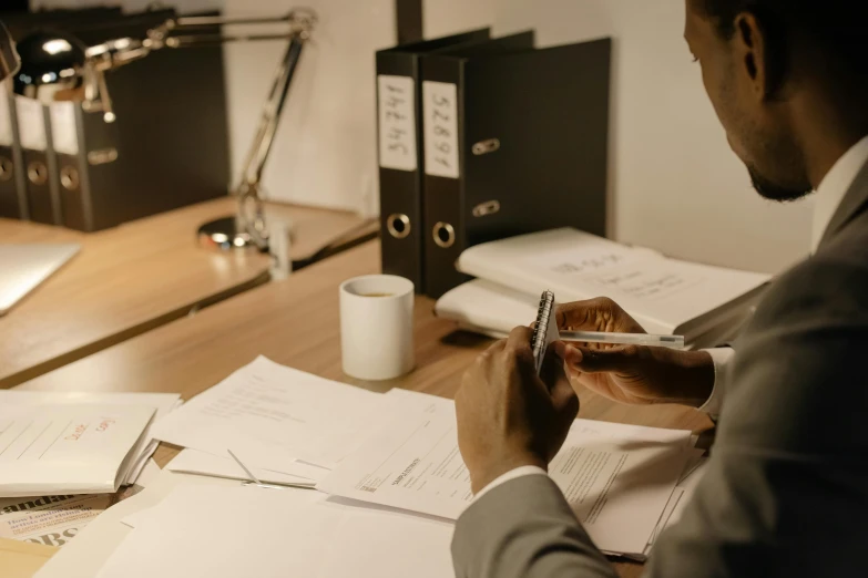 man holding a pen writing on papers with paperwork near by