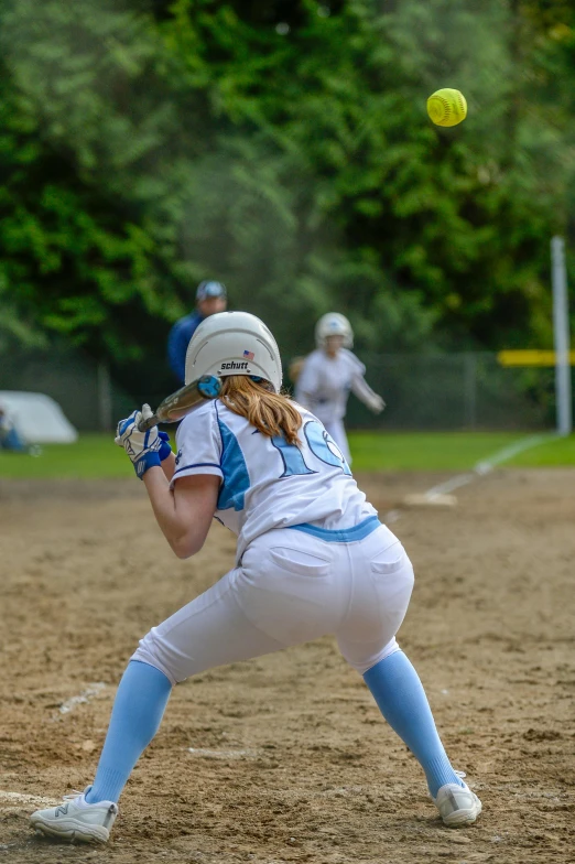 a young woman playing softball with a baseball flying toward her