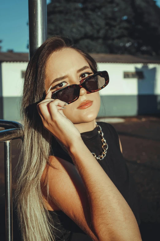 a woman wearing glasses on her head is leaning against a pole