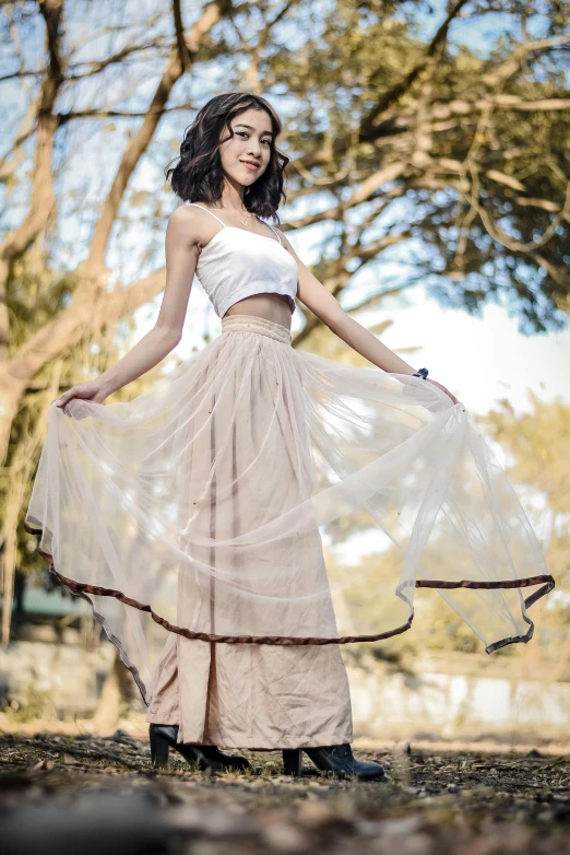 a woman stands in front of trees, her dress is sheerly and her dress is flowing