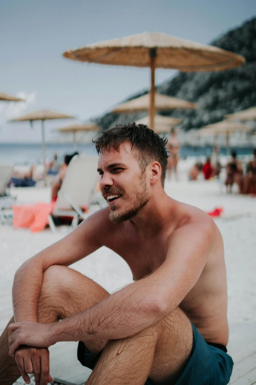 a man sitting on the beach with his knees crossed