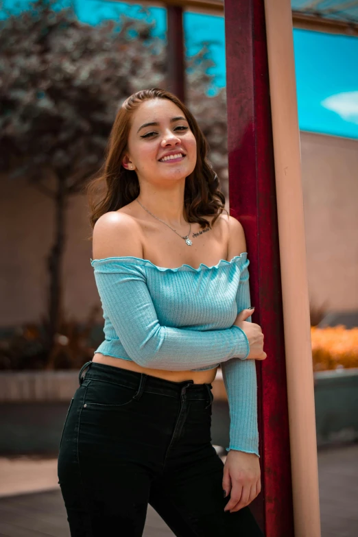 a pretty young lady wearing a blue top standing next to a pole