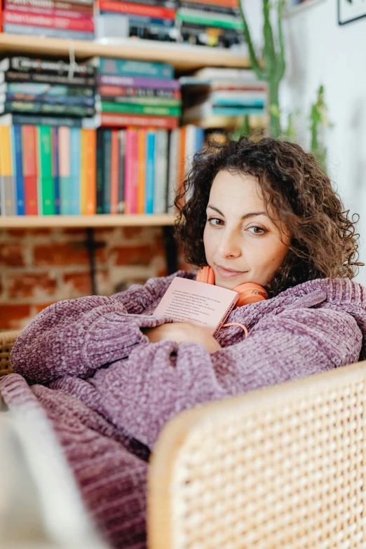 the woman in a blanket is sitting near bookshelves