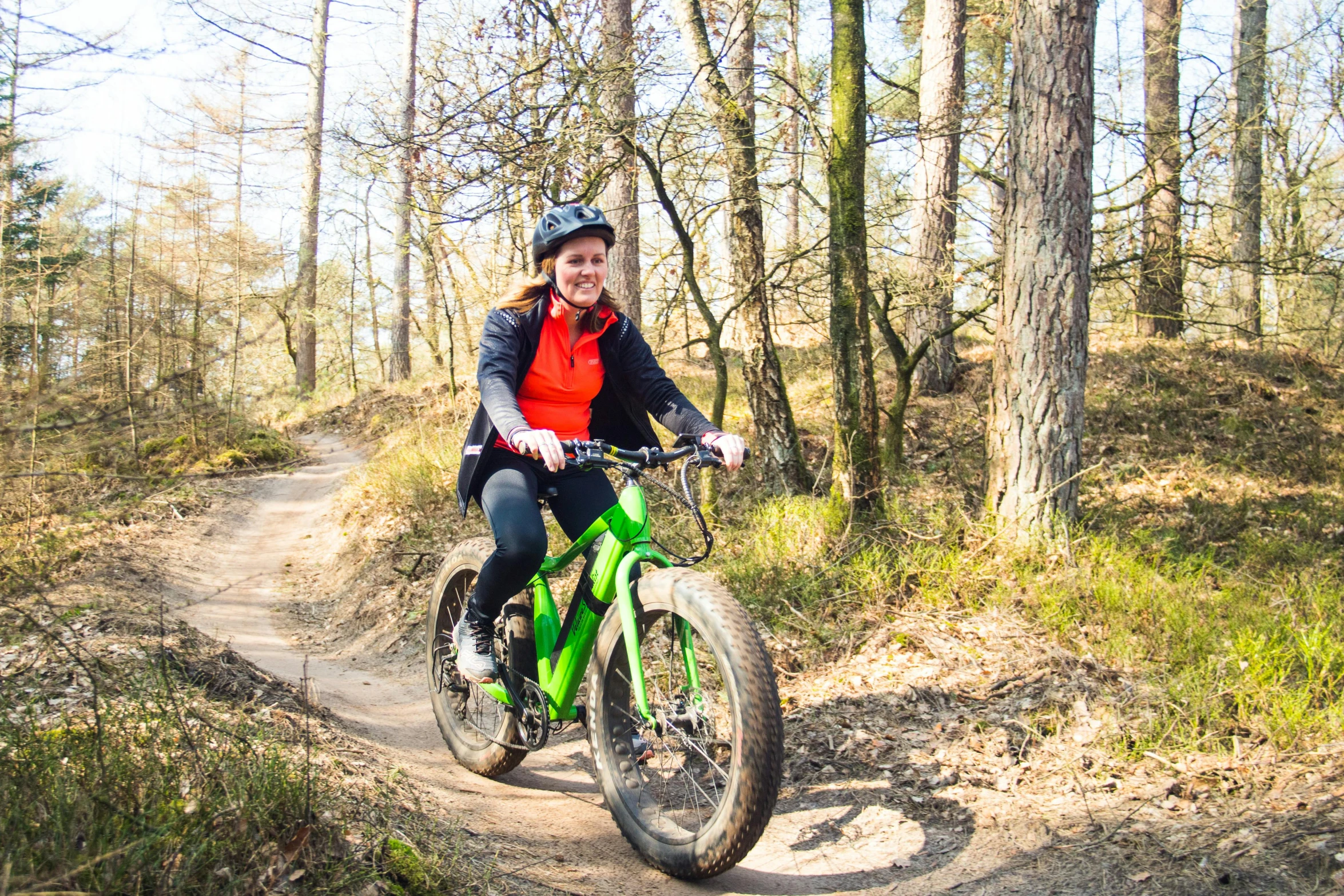 a smiling woman riding a green bicycle on a trail