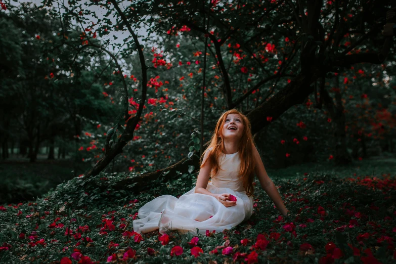 young beautiful red haired girl sitting on the ground surrounded by roses