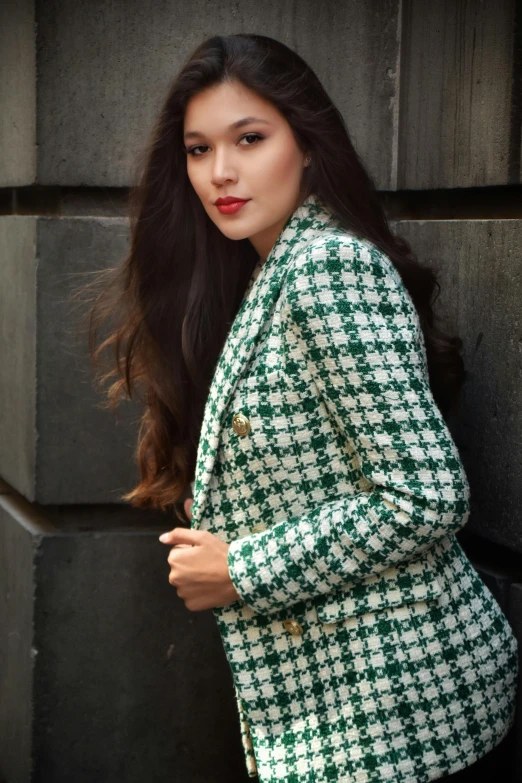 a woman in green and white checkered coat leaning against a building