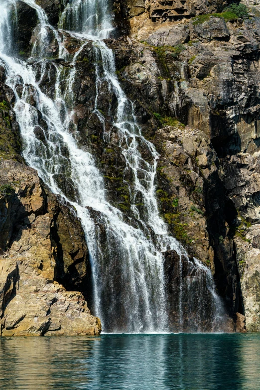 a waterfall falls in a rocky area by the lake