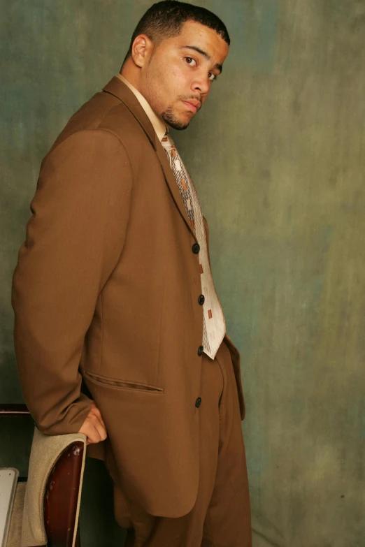 a man wearing a brown suit is posing for the camera