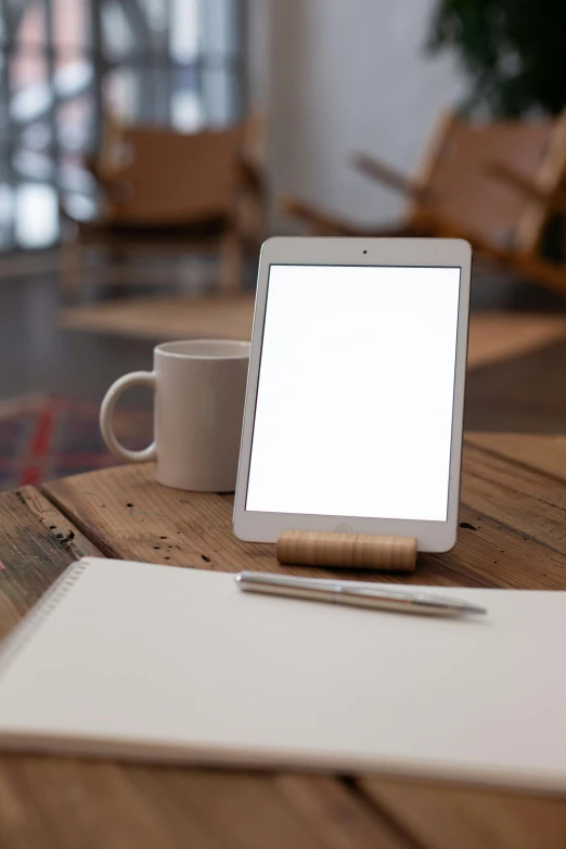 an ipad and a pen and cup on top of a wooden table