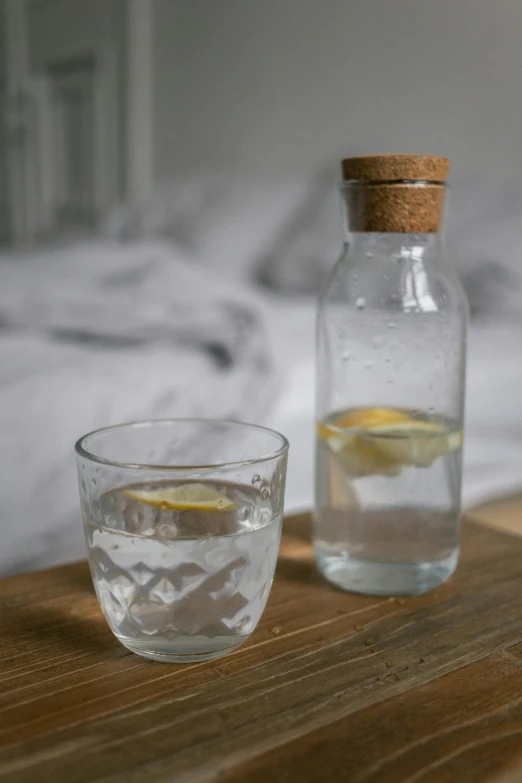 a glass with water next to a bottle filled with lemon