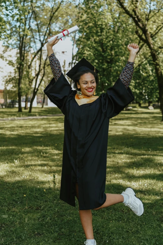 a smiling woman wearing a graduation gown and cap and holding up her graduation cap in the air