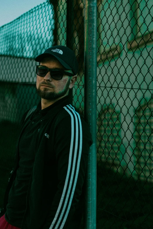 man wearing black and white jacket and sunglasses leaning on fence