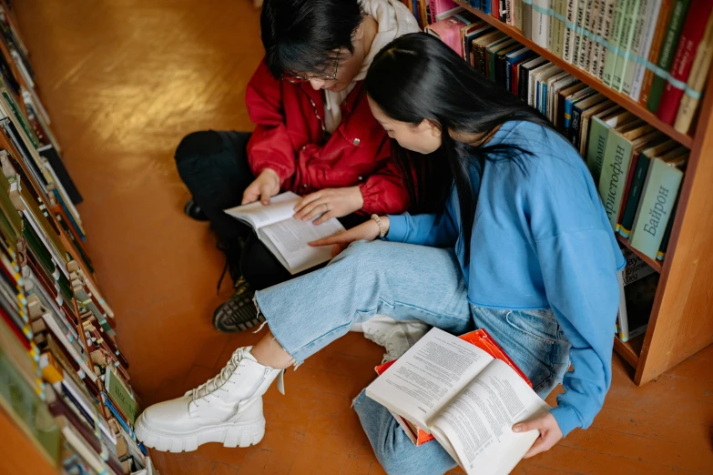 a man and woman sitting on the ground reading books