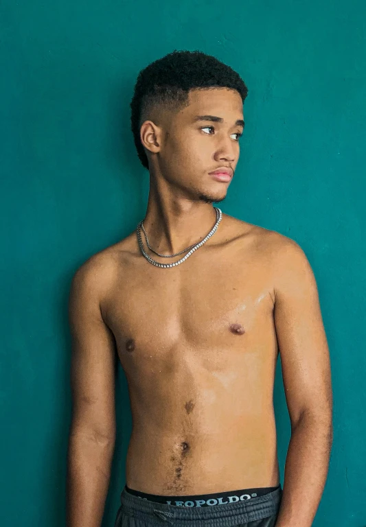 a man wearing a silver chain in front of a turquoise wall