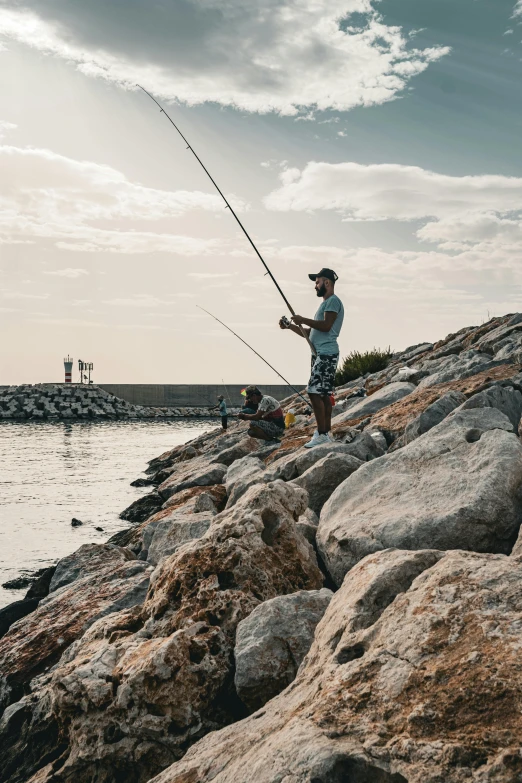 a man standing on rocks next to the ocean while holding onto his fishing rod
