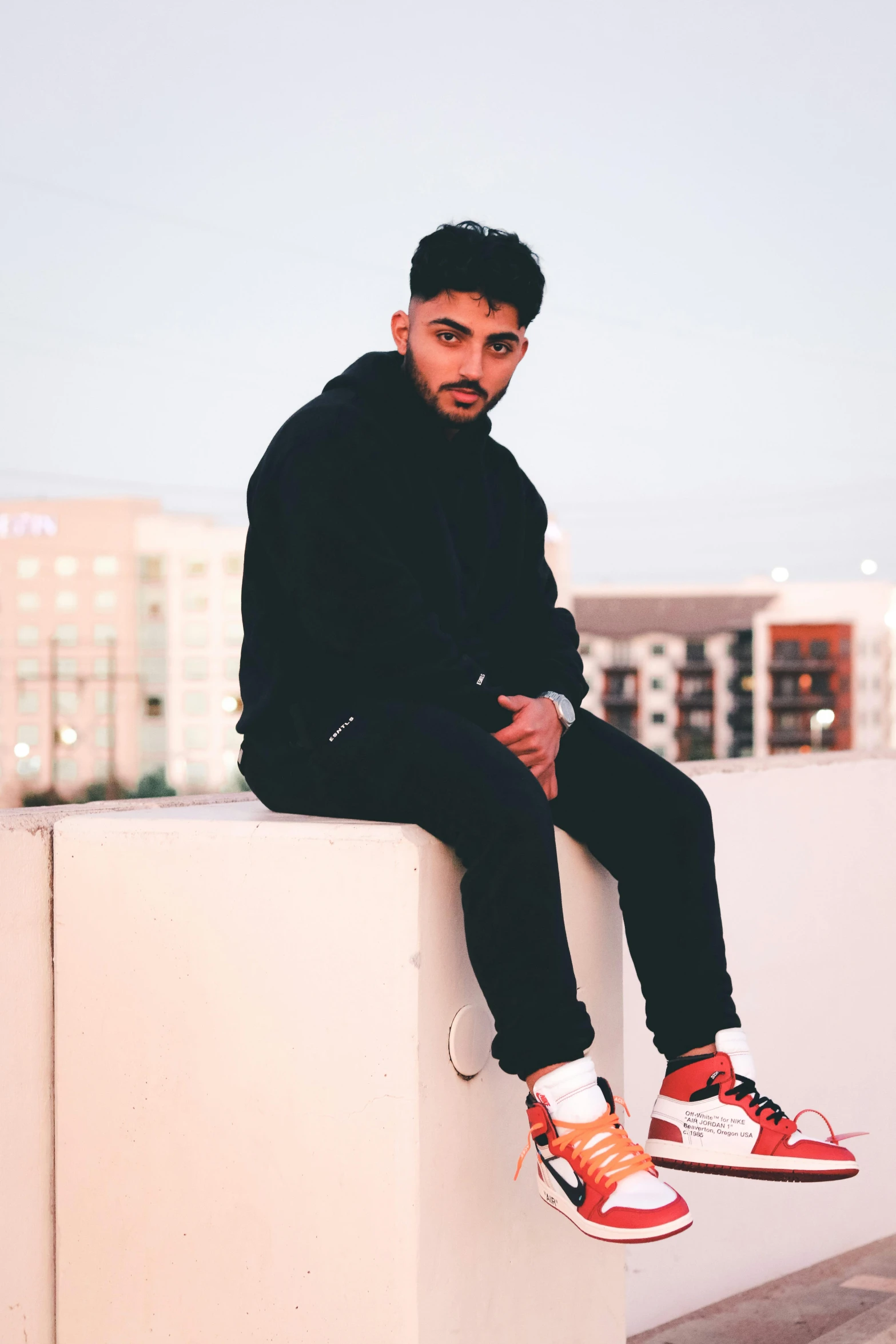 a man with black jacket and hoodie sitting on top of white pillar