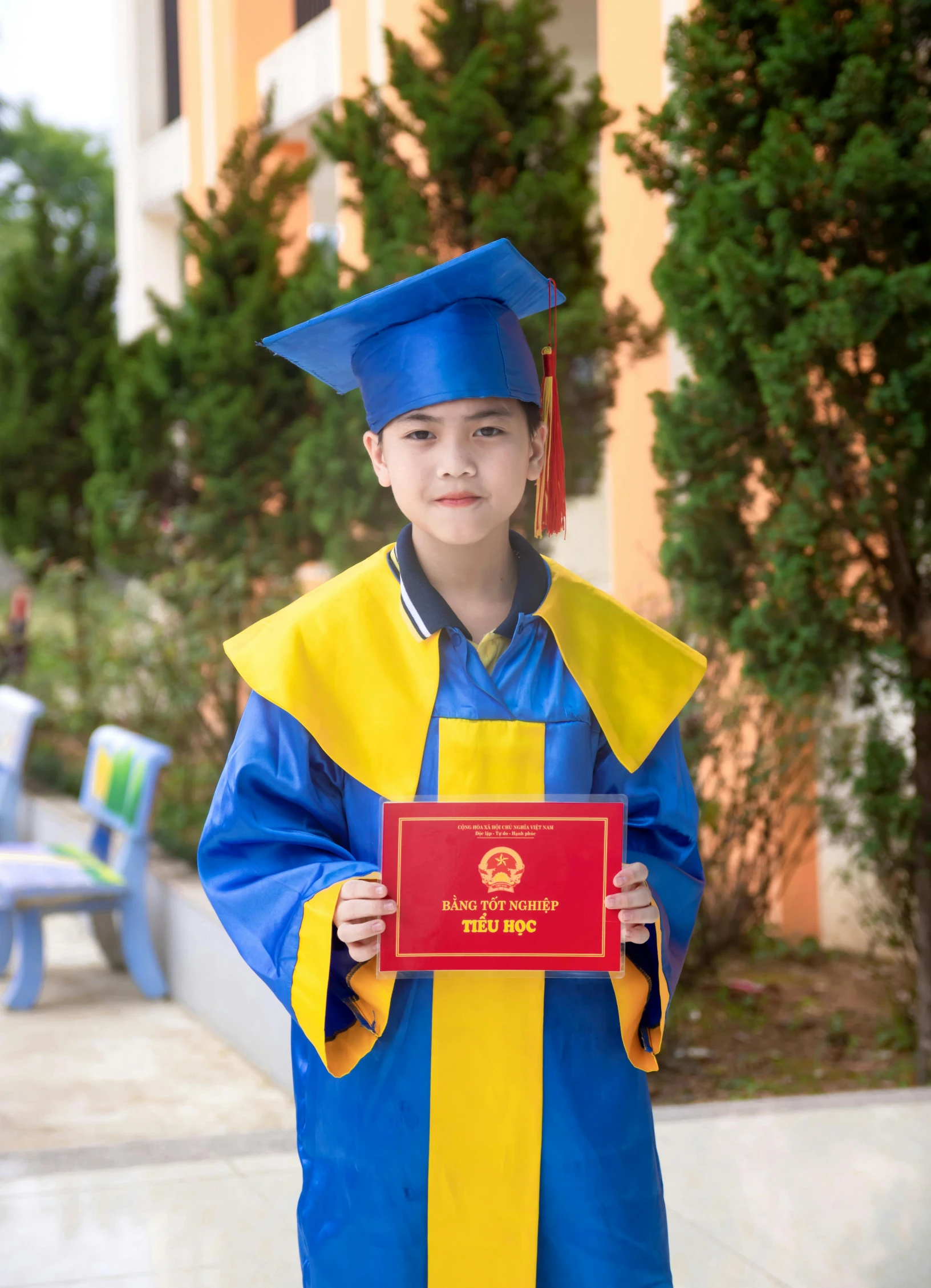 a little boy in blue graduation gown holding up a certificate