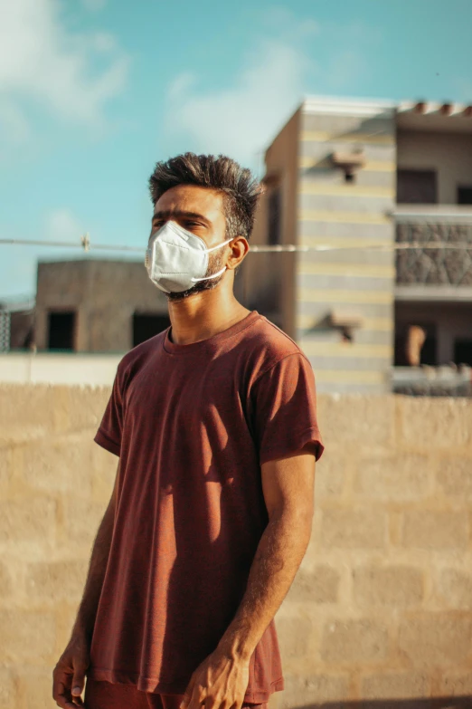 man in red shirt with white mask standing against stone wall