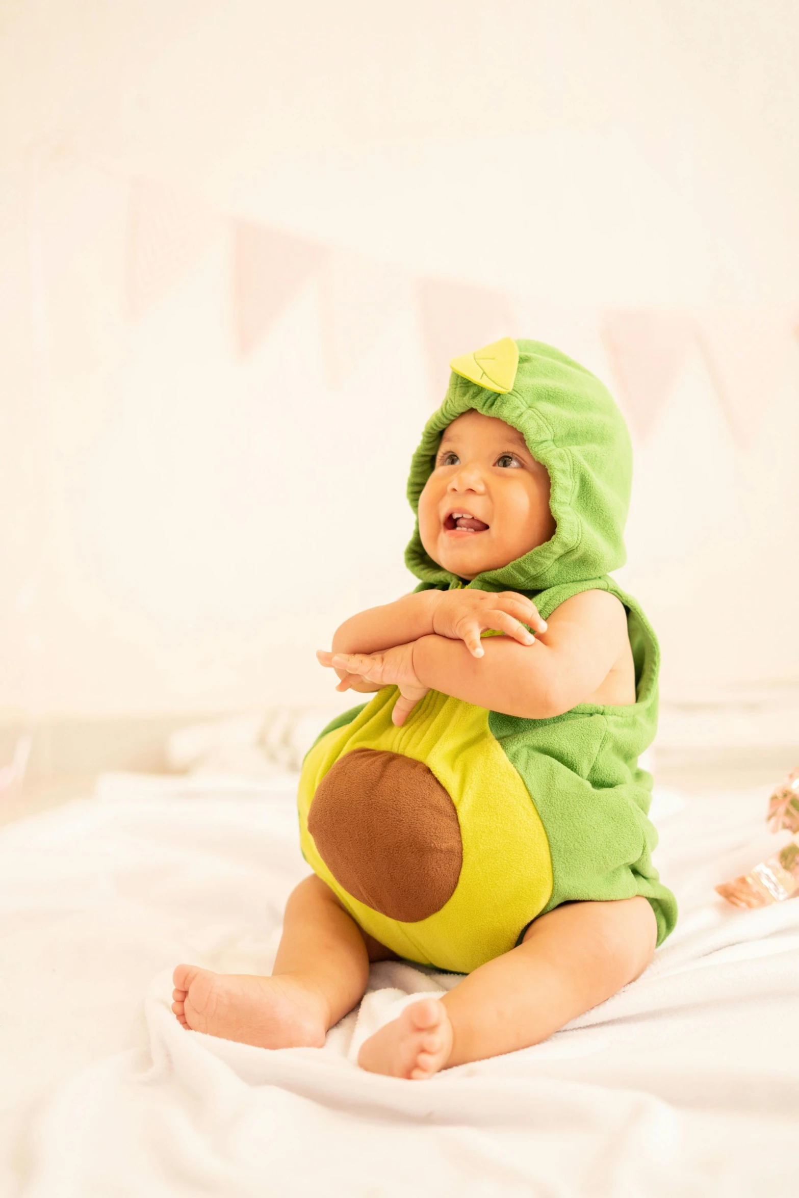 baby in green frog costume sitting on bed