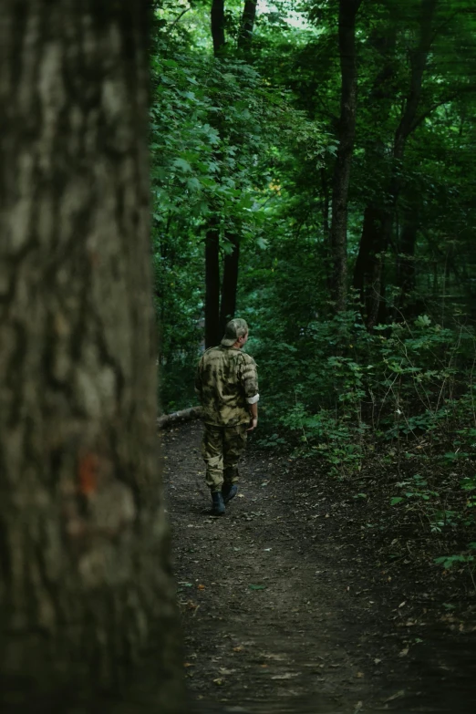 a man in camouflage walks on the trail through the trees