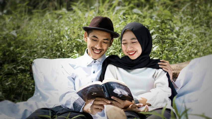 two people sitting on a blanket looking at a book