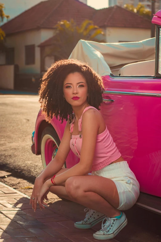 a young woman is sitting on the ground with her foot up against an old pink car