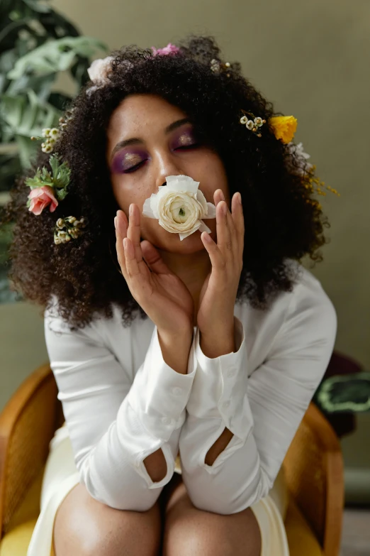 a woman sits in a chair wearing a white shirt and holds her hand to her mouth while she covers her nose