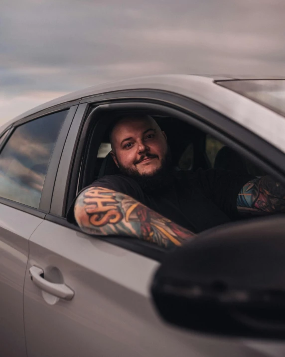 the man is sitting in his car wearing tattoos