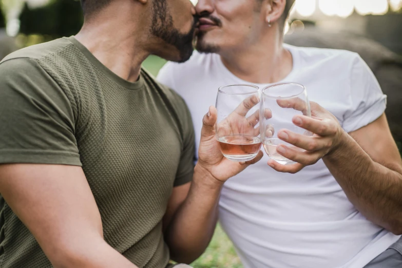 two men share wine glasses for a kiss