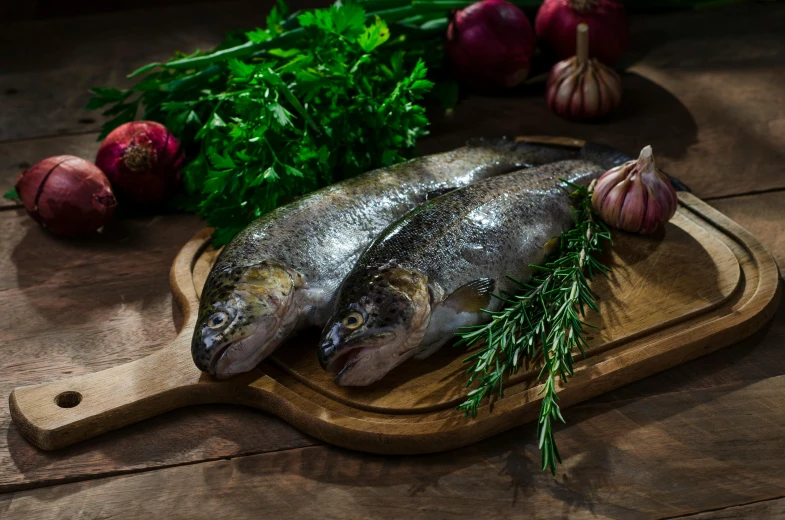 two whole fishes sit on a wooden  board