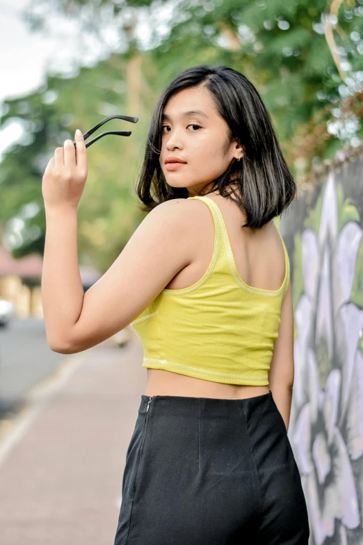 the young woman wearing black high rise leggings is standing outside near graffiti - painted wall and is holding onto her cell phone