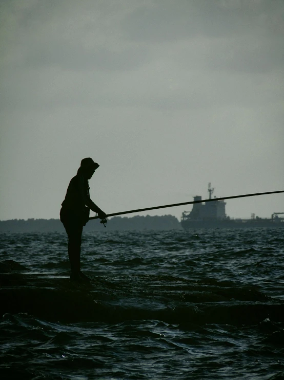 the fisherman stands alone, casting a line into the water