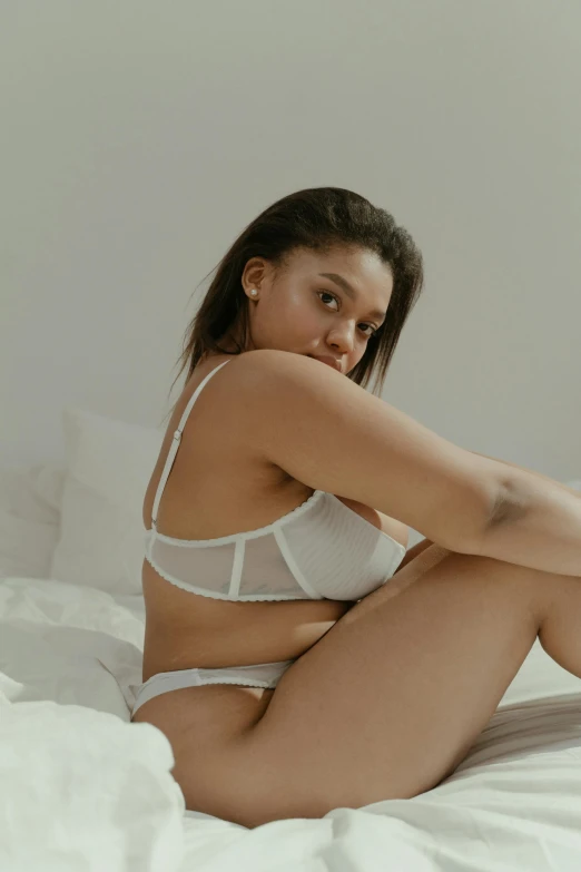 a  woman is sitting on a bed wearing a white lingerie