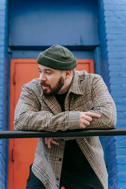 a bearded man leans on a rail, his hands resting on his knee