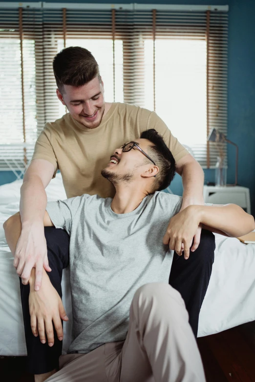 two young men, one in bed hugging while the other sits on his arm