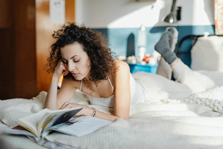 a young woman laying on a bed reading a book