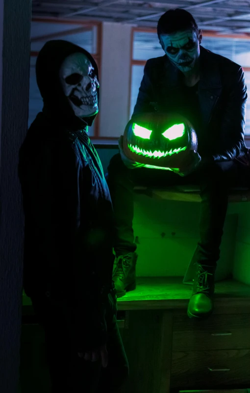 two men sitting down, with glowing lights and masks on their faces