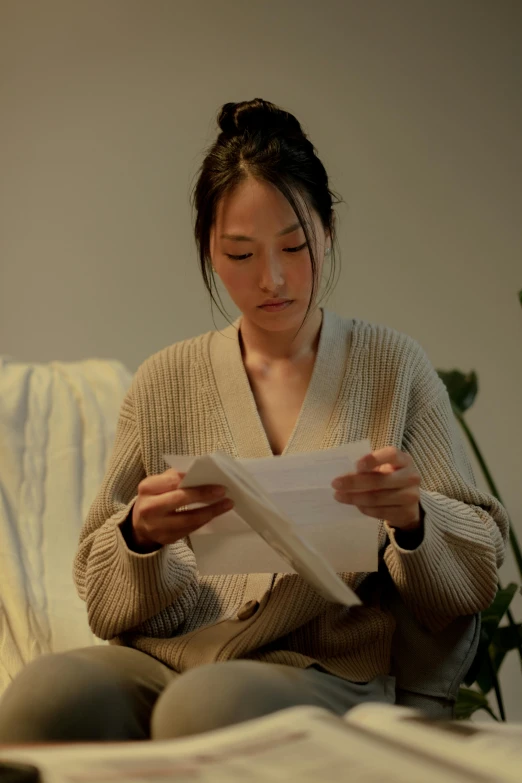 an asian woman sitting on a bed reading paper