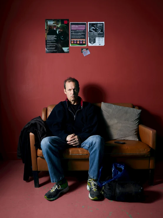 man sitting on leather couch in corner with red walls