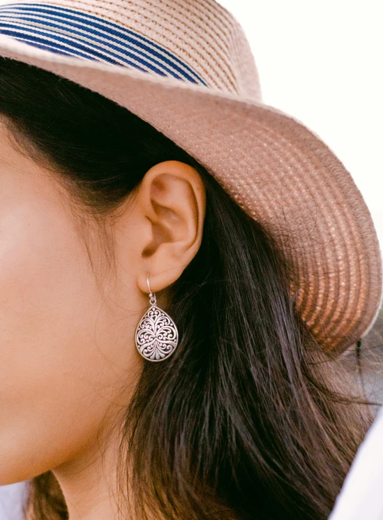 a woman with long hair and a hat has a pair of silver ear studs on her left ear