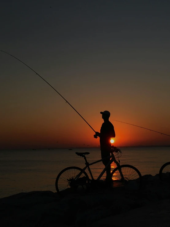 a man stands next to his bike at sunset fishing