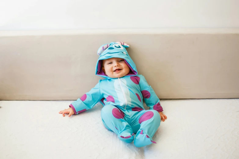 baby in blue pajamas sitting on bed with feet on pillow