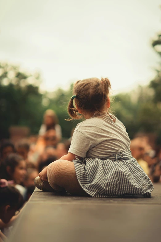 little girl sits on top of a black ledge watching a stage