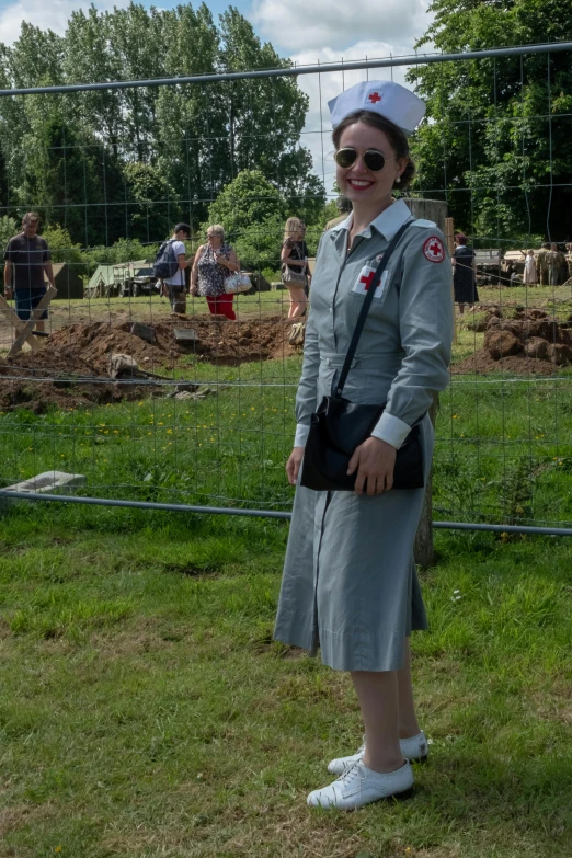 a woman in a grey dress with white top and red emblems on her hat is holding an umbrella