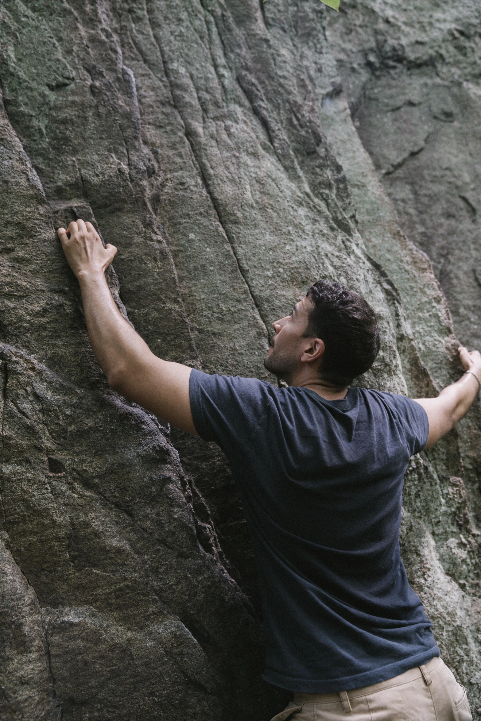 a man in a blue t - shirt on rocks, holding a rock with his right hand