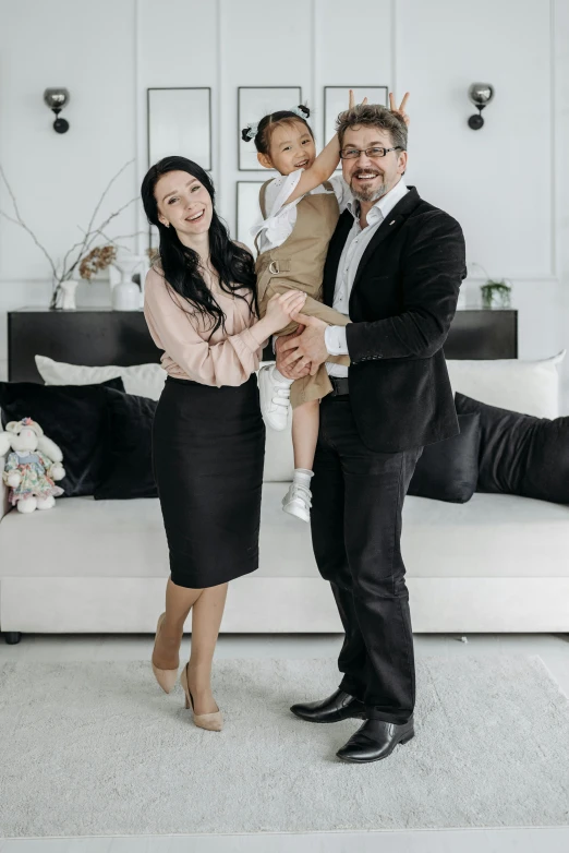 two adults and a child holding a baby posing for a pograph in their white living room